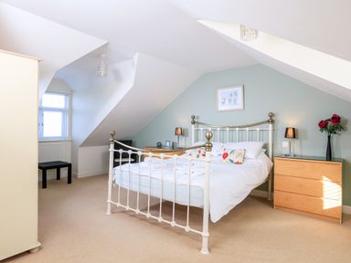 A bedroom with a metal bed frame a wooden dresser with a lamp and flowers and a window with blinds at 2 The Bay in Bigbury
