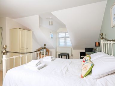 A bedroom with a metal bed frame and white bedding two folded towels on the bed a cream wardrobe wicker chair and a window with blinds at 2 The Bay in Bigbury