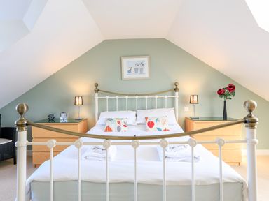 A bedroom with a white metal bed frame two bedside tables with lamps and red flowers on one at 2 The Bay in Bigbury