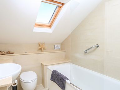 A bathroom with a bathtub a toilet a sink a skylight window and a towel on the bathtub at 2 The Bay in Bigbury