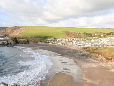 A coastal beach with waves hitting the shore and a village with houses near green fields at 2 The Bay in Bigbury