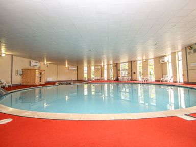 An indoor swimming pool with red carpeted floor and white chairs around at 59 Valley Lodge Callington near Gunnislake