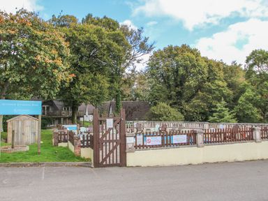 An outdoor swimming pool area with a wooden fence and chairs surrounded by trees at 59 Valley Lodge in Callington near Gunnislake