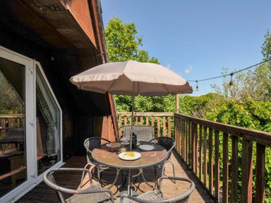 A wooden balcony with a round table and four chairs under a large umbrella at 59 Valley Lodge in Callington near Gunnislake