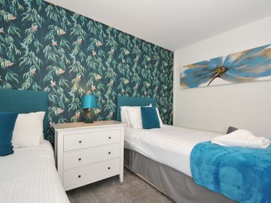 A bedroom with two single beds a white chest of drawers and a lamp at 59 Valley Lodge in Callington near Gunnislake