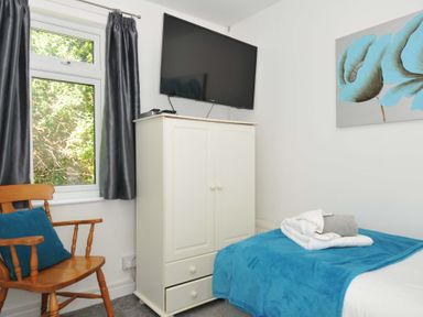 A bedroom with a wooden chair a blue cushion a white wardrobe a wall mounted television and a bed with blue bedding and folded towels at 59 Valley Lodge Callington near Gunnislake