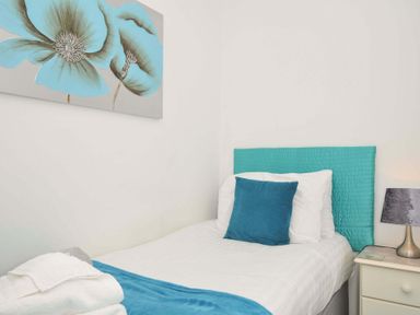 A bedroom with a single bed with blue headboard and cushion next to a bedside table with a lamp at 59 Valley Lodge in Callington near Gunnislake