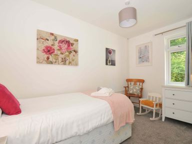 A bedroom with a single bed a wooden chair a small rocking chair a chest of drawers and artwork on the walls at 59 Valley Lodge in Callington near Gunnislake