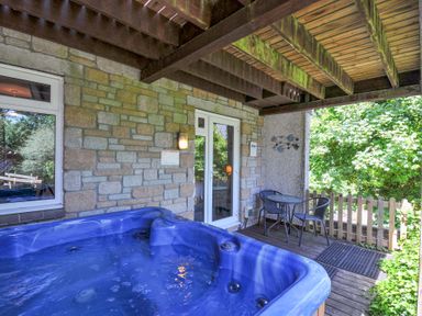 An outdoor patio with a blue hot tub a small table with two chairs wooden deck and stone wall at 59 Valley Lodge in Callington near Gunnislake
