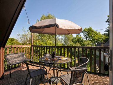 A wooden balcony with a round table under an umbrella and four chairs at 59 Valley Lodge in Callington near Gunnislake
