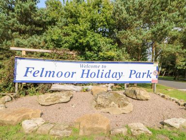 A welcome sign for Felmoor Holiday Park surrounded by trees and large rocks at Jalan End in Felton