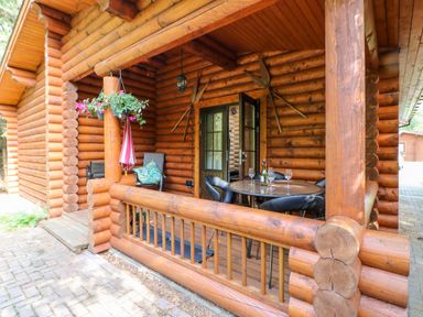 A wooden porch with a round table and chairs and hanging flower pots at a log cabin at Jalan End in Felton