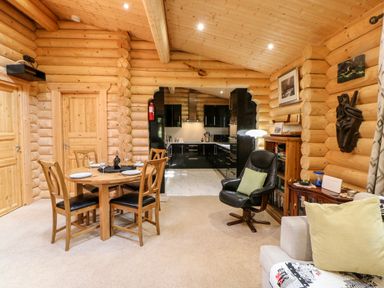 A wooden dining table with four chairs set with plates and glasses near a log cabin style kitchen with black cabinets and a black armchair in a living area at Jalan End in Felton