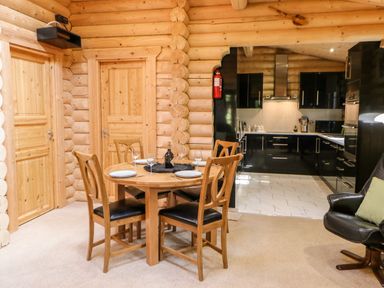 A dining area with a round wooden table and four chairs set with plates and glasses next to a kitchen with black cabinets at Jalan End in Felton