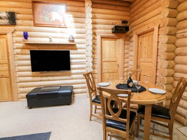 A dining area with a wooden round table set with plates and glasses next to a television mounted on a log wall at Jalan End in Felton