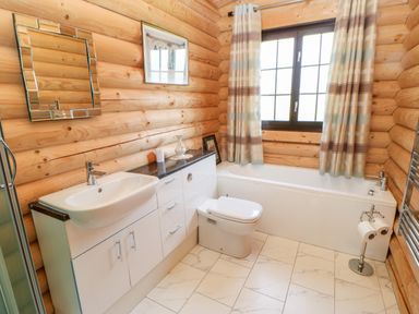 A bathroom with a sink, toilet, bathtub, mirror, window with curtains, and wooden log walls at Jalan End in Felton