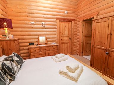 A bedroom with wooden log walls a bed with folded towels wooden furniture and a lamp at Jalan End in Felton