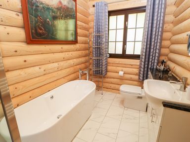 A bathroom with a bathtub toilet sink wooden log walls tiled floor and a window with curtains at Jalan End in Felton