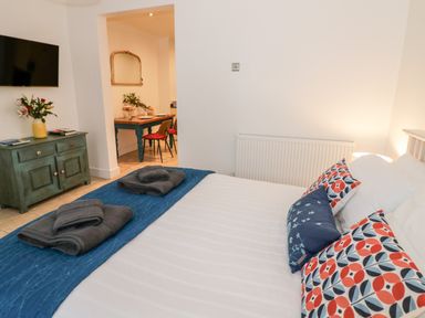 A bedroom with a bed and folded towels a cabinet with flowers and a TV and a dining area at The Hideaway in Malvern