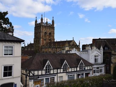 A historic stone church with a tall tower behind older buildings in a town at The Hideaway in Malvern