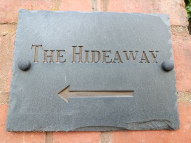 A stone sign with THE HIDEAWAY and an arrow pointing left on a brick wall at The Hideaway in Malvern