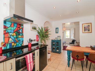 A kitchen with a colorful stained glass backsplash a wooden dining table with chairs and a blue cabinet at The Hideaway in Malvern