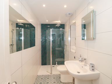A bathroom with a sink, toilet, glass shower enclosure, patterned floor tiles and green tiles in the shower area at The Hideaway in Malvern