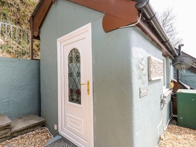 Exterior corner of a small building with a white door featuring decorative glass at The Nook Star near Cenarth