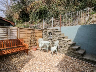 An outdoor patio area with wooden bench metal table and chairs stone steps and a statue at The Nook Star near Cenarth