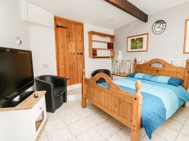 A bedroom with a wooden bed blue bedding a black chair a wooden door a wall clock and a television at The Nook Star near Cenarth