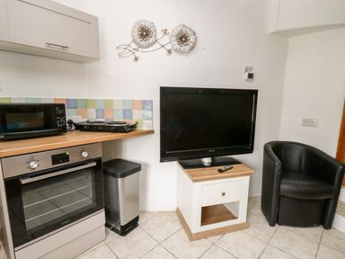 A kitchen corner with an oven microwave trash can television on a small table and a black chair at The Nook in Star near Cenarth