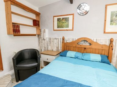 A bedroom with a wooden bed and blue bedding a black chair a wooden shelf with books and framed pictures on the wall at The Nook Star near Cenarth