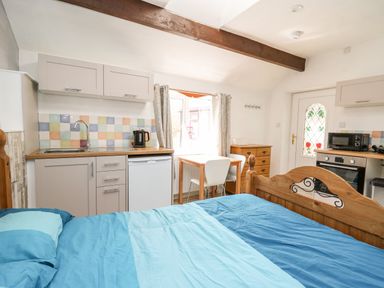 A small room with a bed a kitchenette with cabinets a fridge kettle and oven a wooden dresser a table with two chairs and a door with floral stained glass at The Nook Star near Cenarth