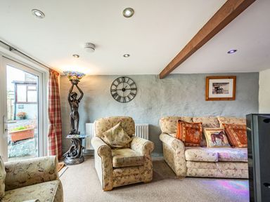 A living room with patterned armchairs and sofa a statue lamp a clock and a framed photo at Pendre Cottage in Cenarth