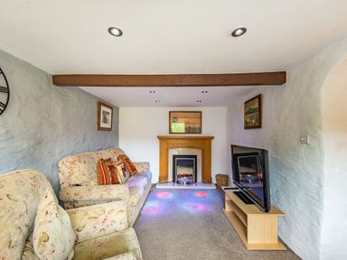 A living room with floral sofas a fireplace a television on a stand and framed pictures on the walls at Pendre Cottage in Cenarth