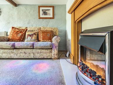 A living room with a floral sofa with animal print cushions and a fireplace at Pendre Cottage in Cenarth