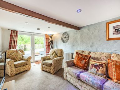 A living room with floral armchairs and sofa near glass doors with plaid curtains at Pendre Cottage in Cenarth