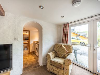 An armchair next to glass patio doors with a view of a yellow car outside at Pendre Cottage in Cenarth