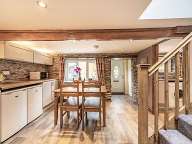 A kitchen dining area with wooden table and chairs stone walls and wooden staircase at Pendre Cottage in Cenarth