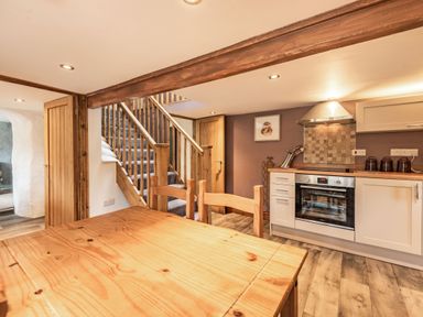 A kitchen and dining area with wooden table and chairs wooden stairs and integrated oven at Pendre Cottage in Cenarth