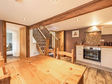 A kitchen with wooden dining table chairs oven and stairs in the background at Pendre Cottage in Cenarth