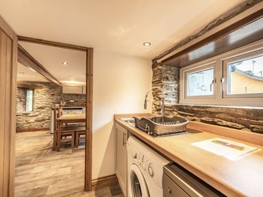 A kitchen area with a washing machine sink and drying rack next to a window and a dining area with a wooden table and chairs at Pendre Cottage in Cenarth
