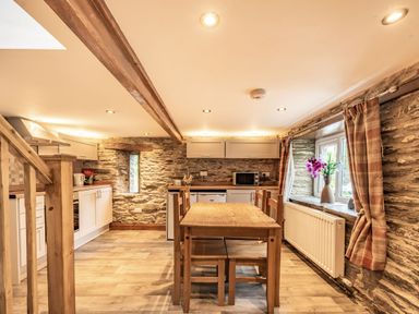 A kitchen with a wooden dining table and chairs stone walls and a window with curtains at Pendre Cottage in Cenarth