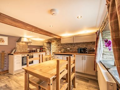 A kitchen with wooden dining table and chairs stone walls and cabinets with appliances at Pendre Cottage in Cenarth