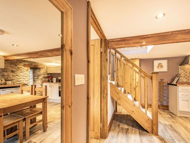 A kitchen and dining area with wooden table and chairs and a wooden staircase at Pendre Cottage in Cenarth