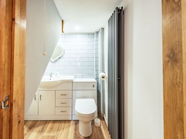A bathroom with a toilet sink and cabinet under a slanted ceiling at Pendre Cottage in Cenarth