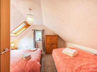 A bedroom with two beds with folded towels a small wooden wardrobe and a window at Pendre Cottage in Cenarth