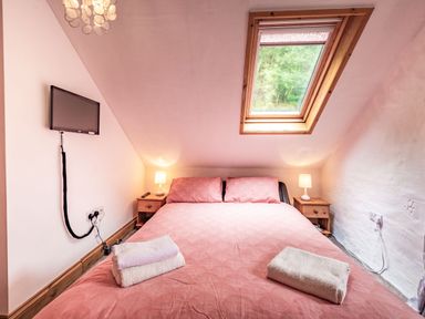 A bedroom with a double bed with pink bedding and two bedside tables with lamps under a skylight window at Pendre Cottage in Cenarth