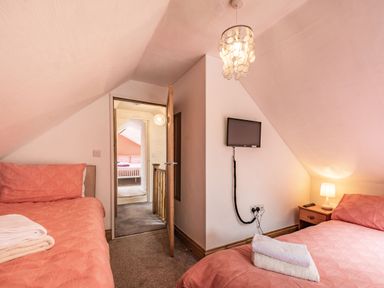 A bedroom with two single beds with coral bedding a small wall-mounted TV and a wooden nightstand with a lamp at Pendre Cottage in Cenarth