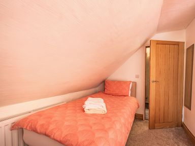 A small bedroom with a single bed with orange bedding and folded towels on the bed at Pendre Cottage in Cenarth